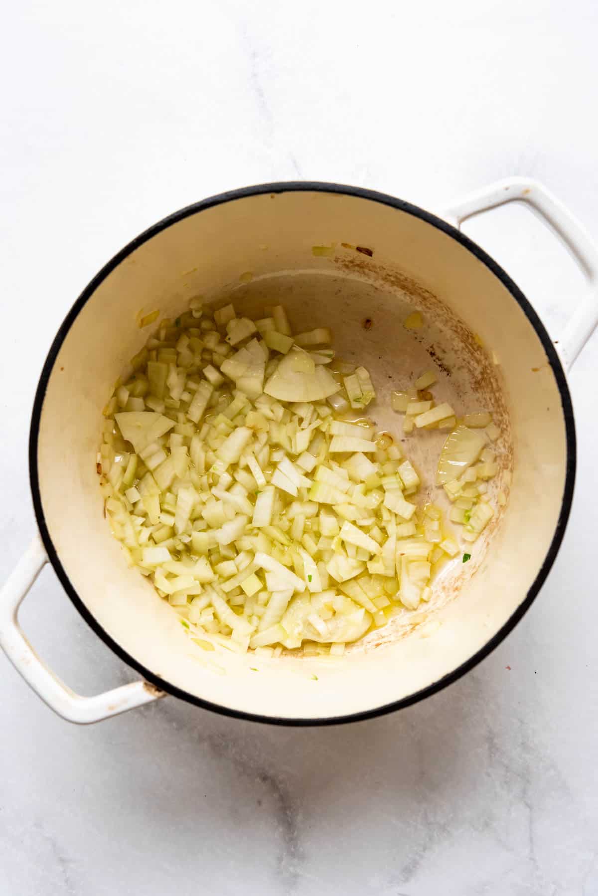 Sauteeing chopped onions in olive oil in a large dutch oven.