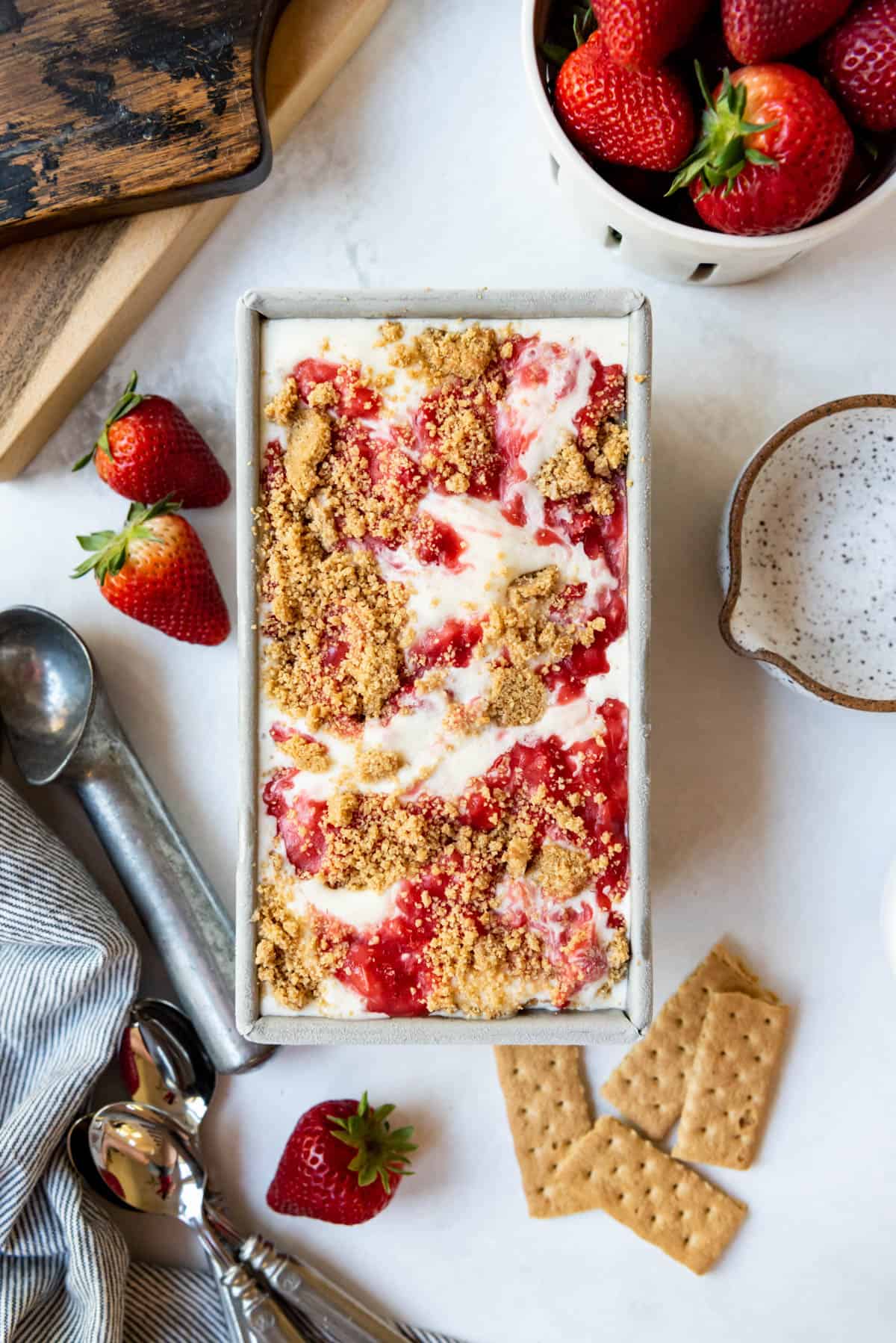 Top view of a metal pan filled with ice cream, strawberry sauce, and graham cracker crumbs.