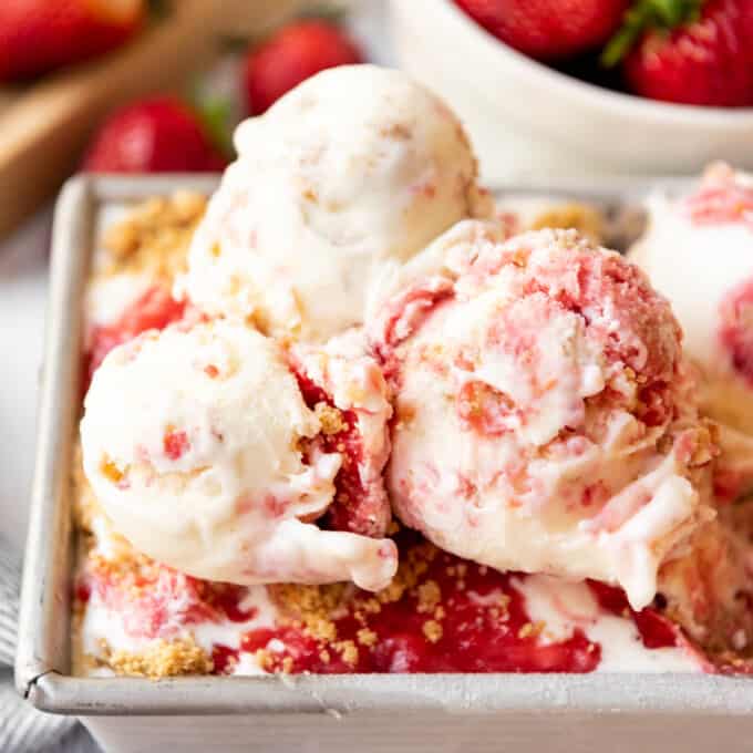 Scoops of strawberry cheesecake ice cream next to graham crackers and strawberries.