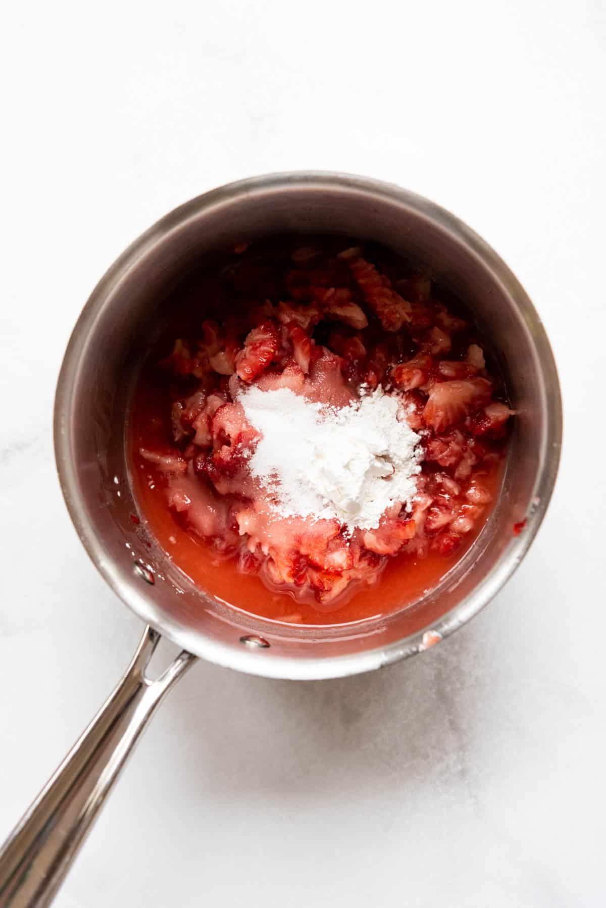 Top view of a saucepan with strawberries, sugar, and cornstarch in it.