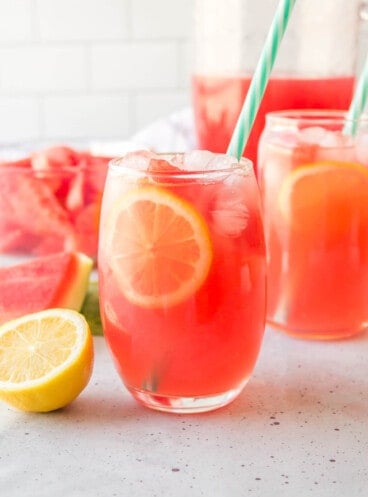 A glass of watermelon lemonade with a striped blue and white straw.