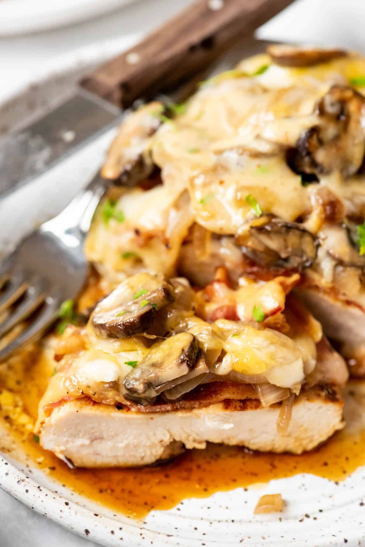 A slice of moist chicken breast topped with melted cheese, mushrooms, and bacon.