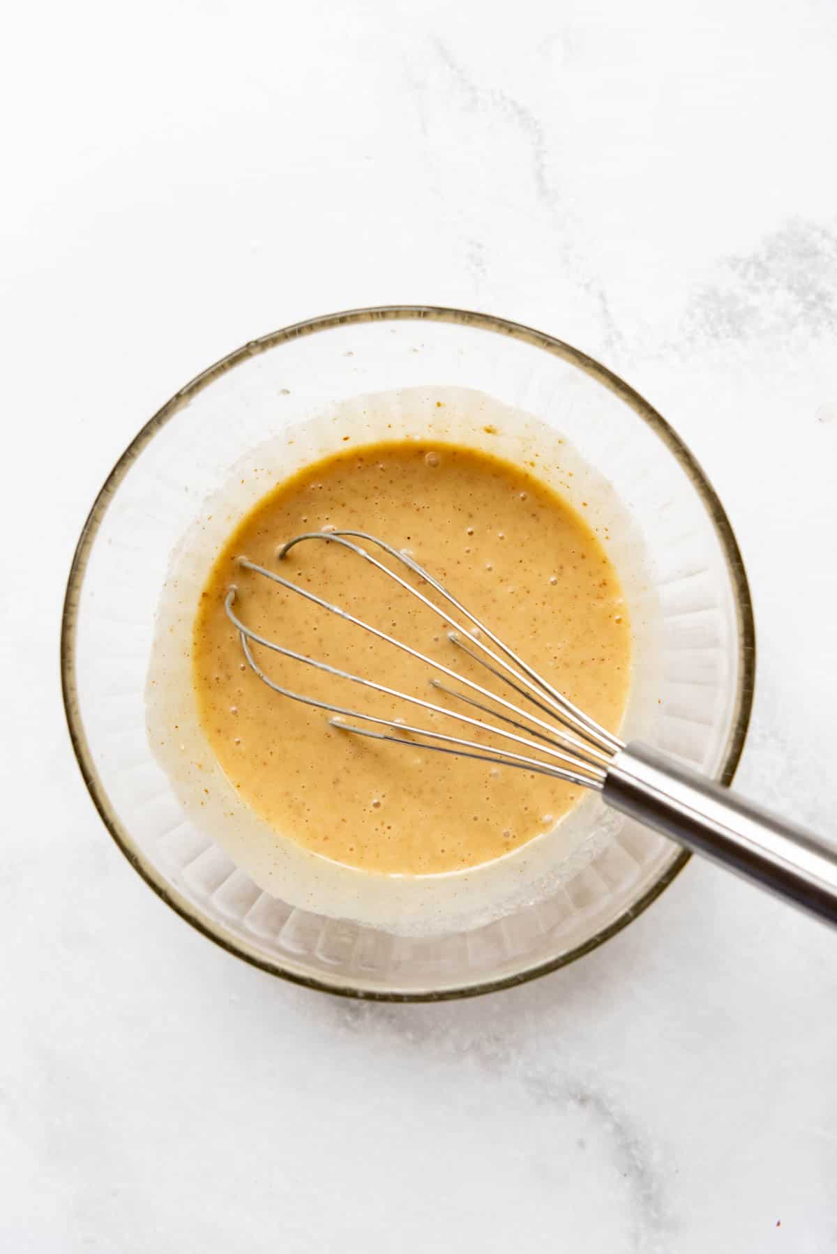 Honey mustard marinade in a glass bowl with a whisk.