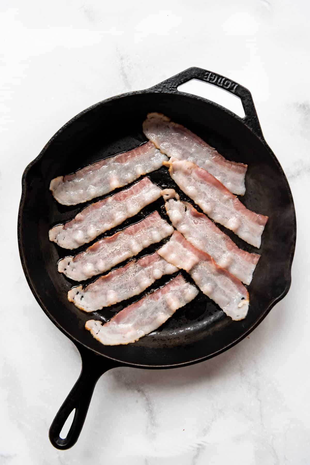 Cooking bacon slices in a cast iron skillet.