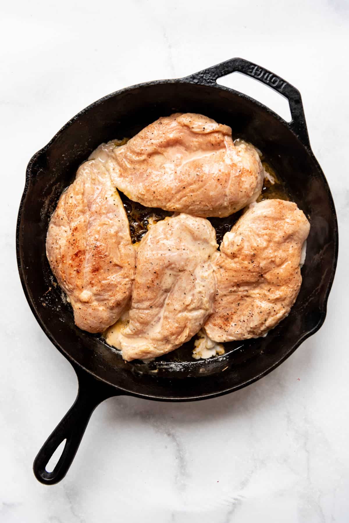 Adding marinated chicken breasts to a cast iron pan.
