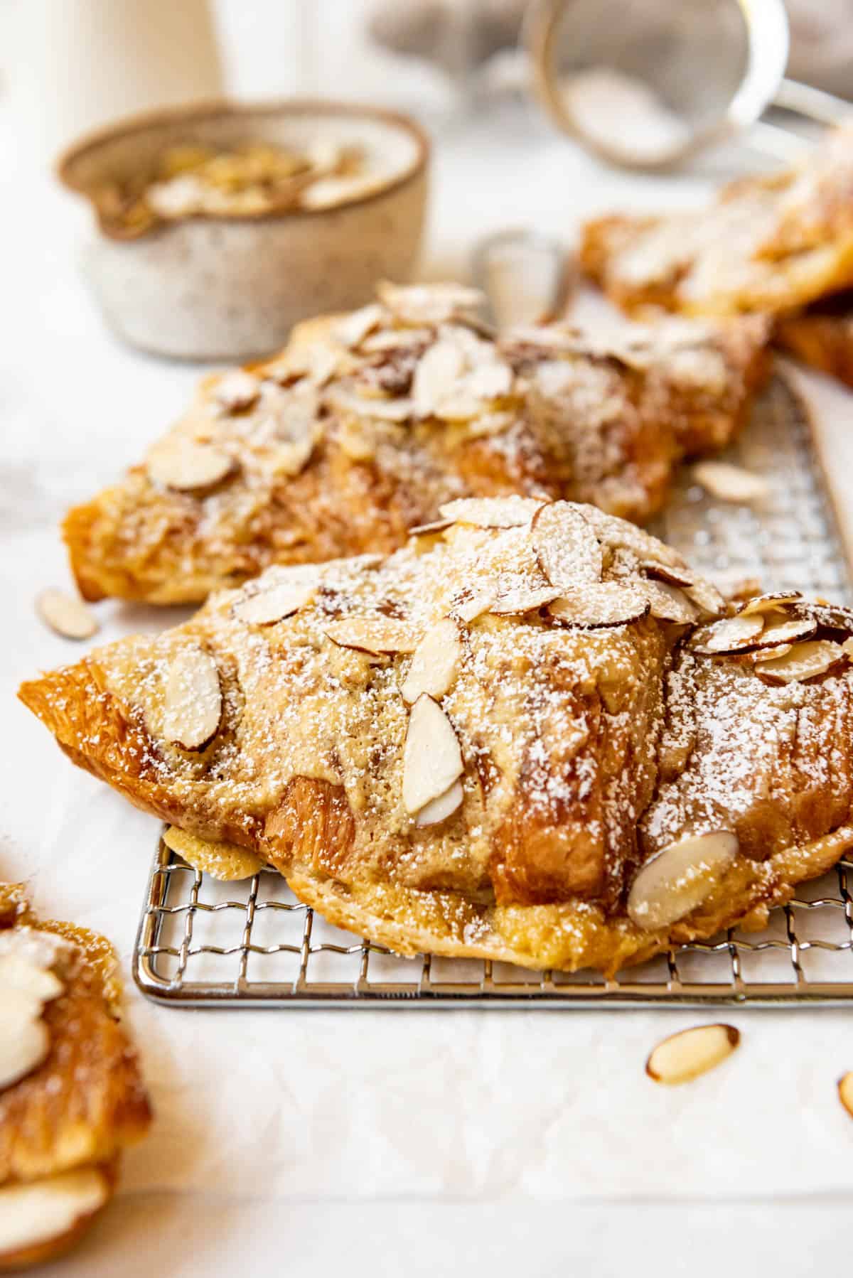 A rich semi-homemade almond croissant on a wire rack topped with slivered almonds and dusted with powdered sugar.