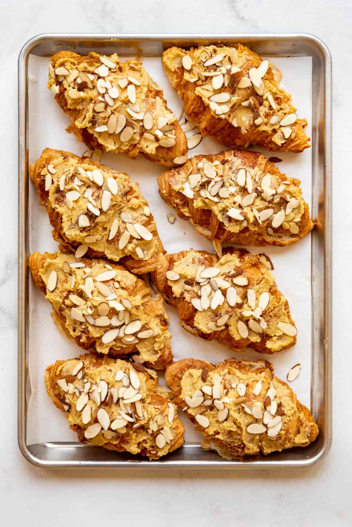 Sprinkling sliced almonds on top of almond croissants on a baking sheet.