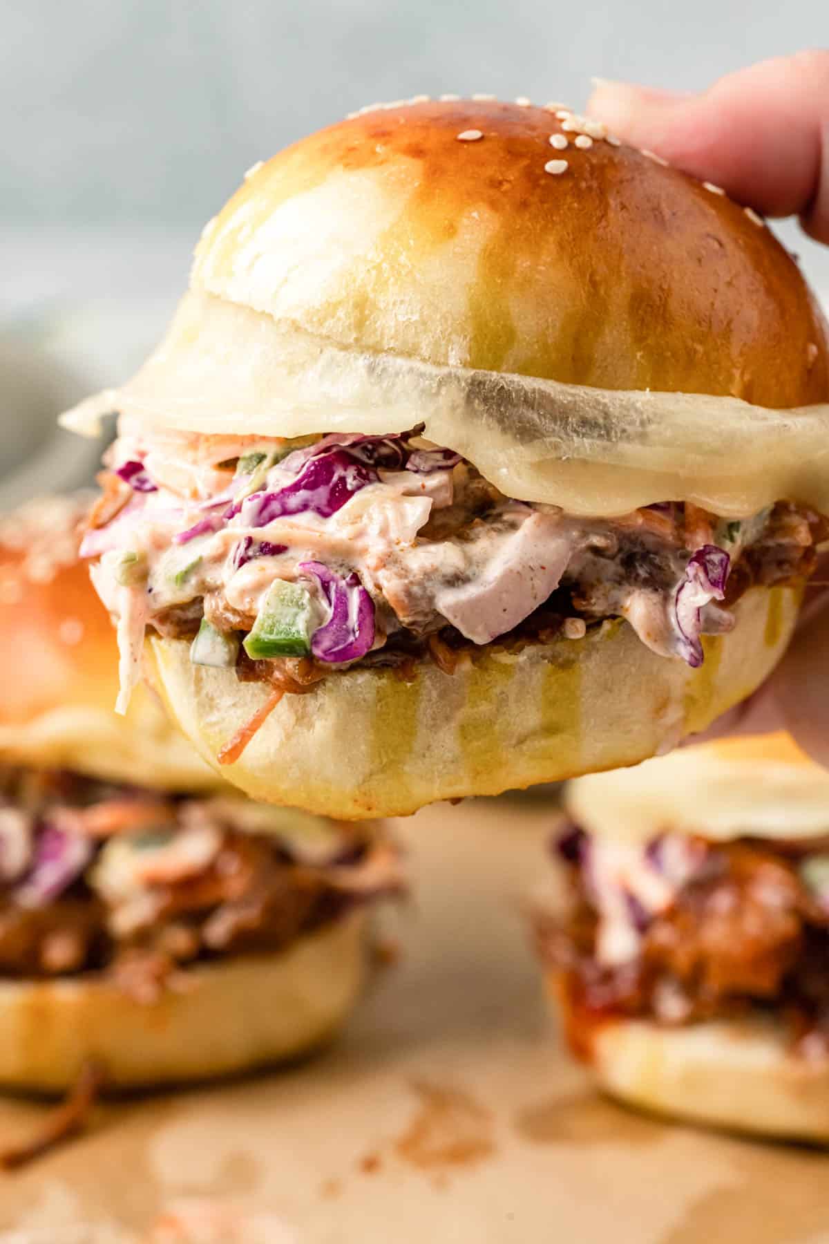 A hand holding a brisket sandwich with coleslaw and provolone cheese.