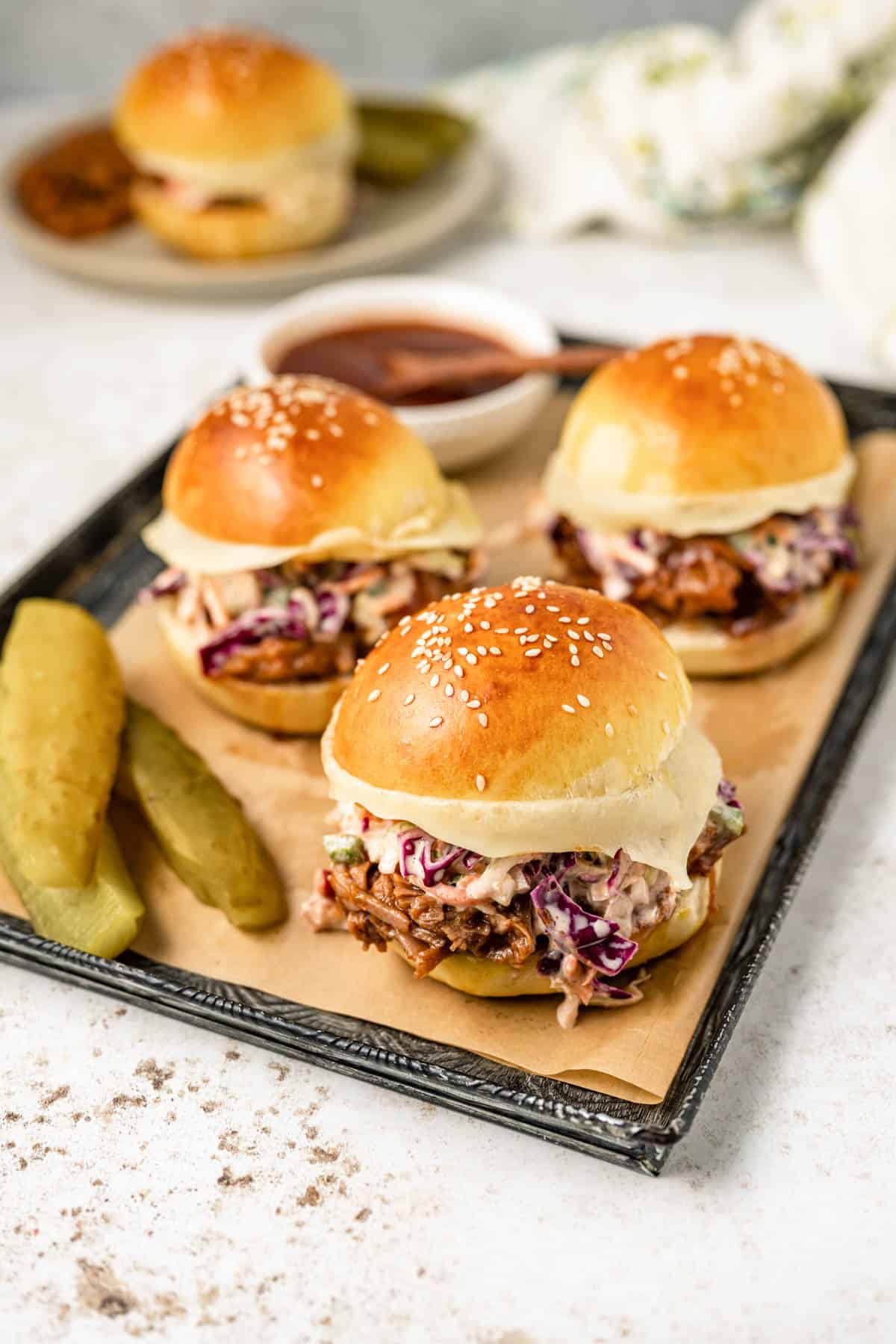 Three beef brisket sandwiches with some dill pickle spears beside them.