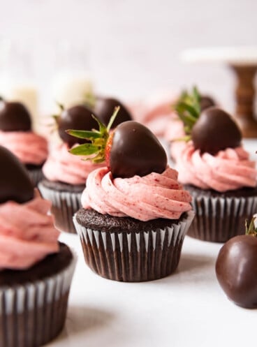 Chocolate cupcakes decorated with tall swirls of piped strawberry frosting and chocolate covered strawberries.