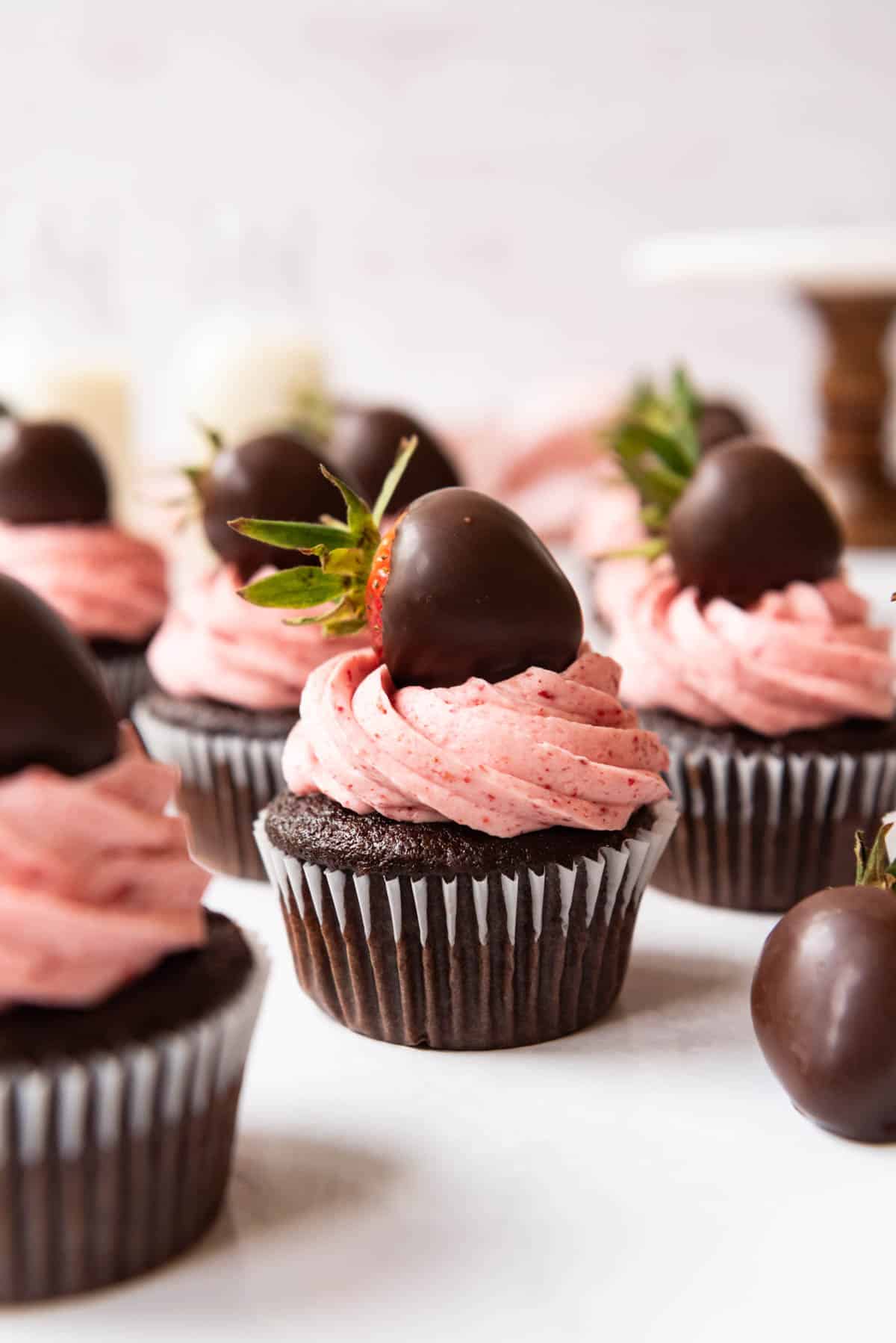 Chocolate cupcakes decorated with tall swirls of piped strawberry frosting and chocolate covered strawberries.