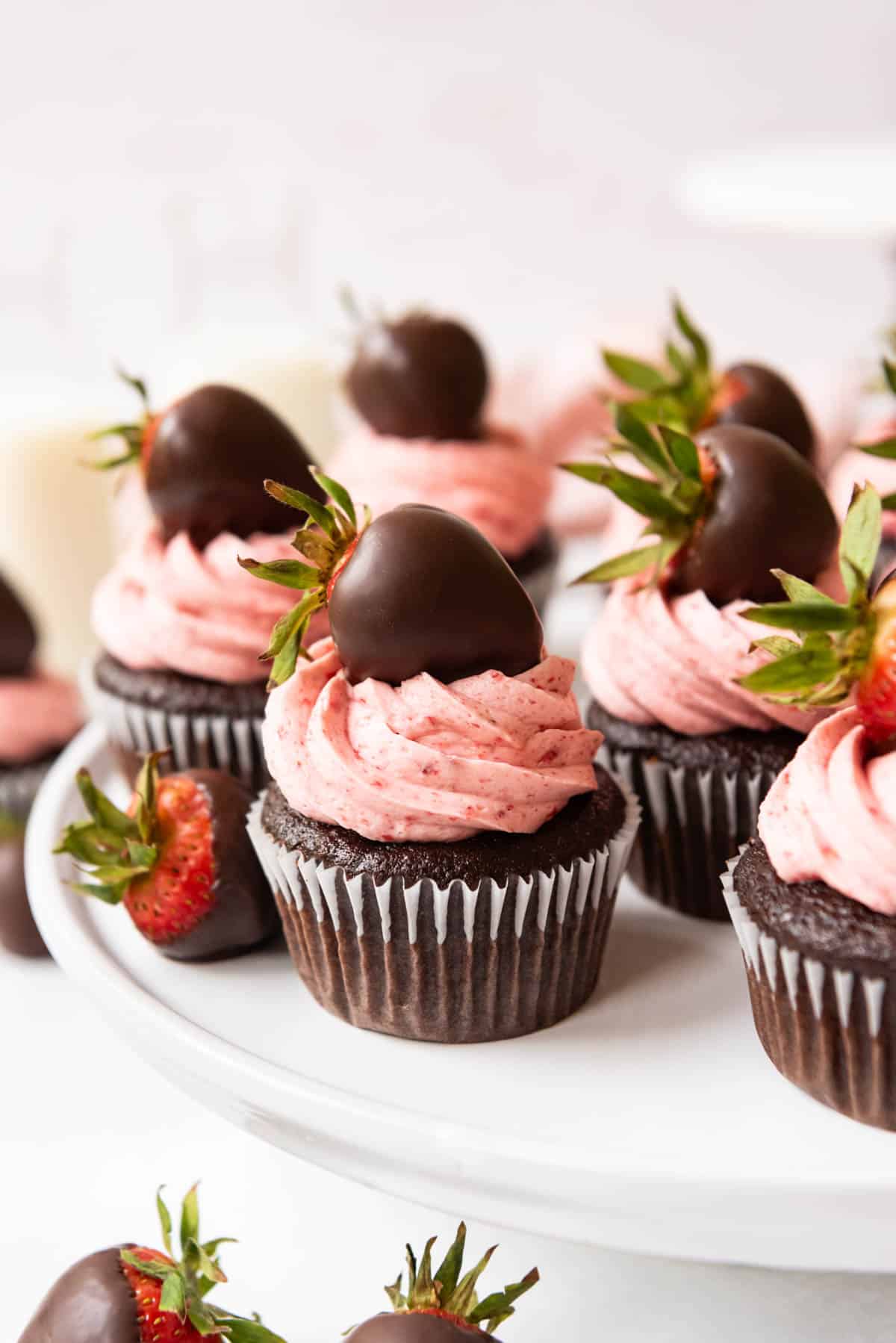 Chocolate covered strawberry cupcakes on a white cake stand.
