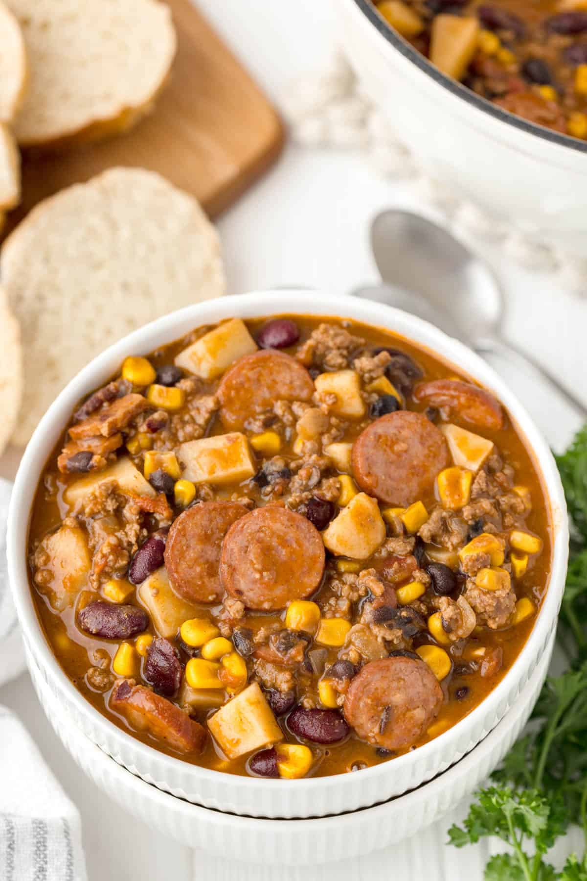 A bowl of thick cowboy stew with sliced bread in the back.