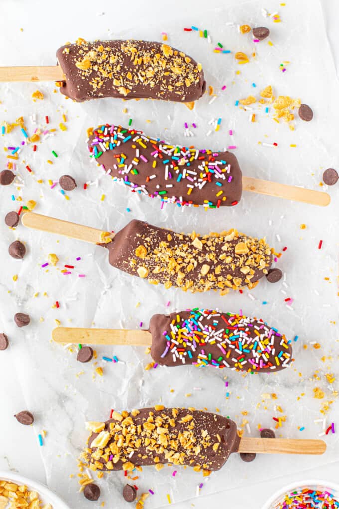 An overhead image of five frozen banana pops on white parchment paper.