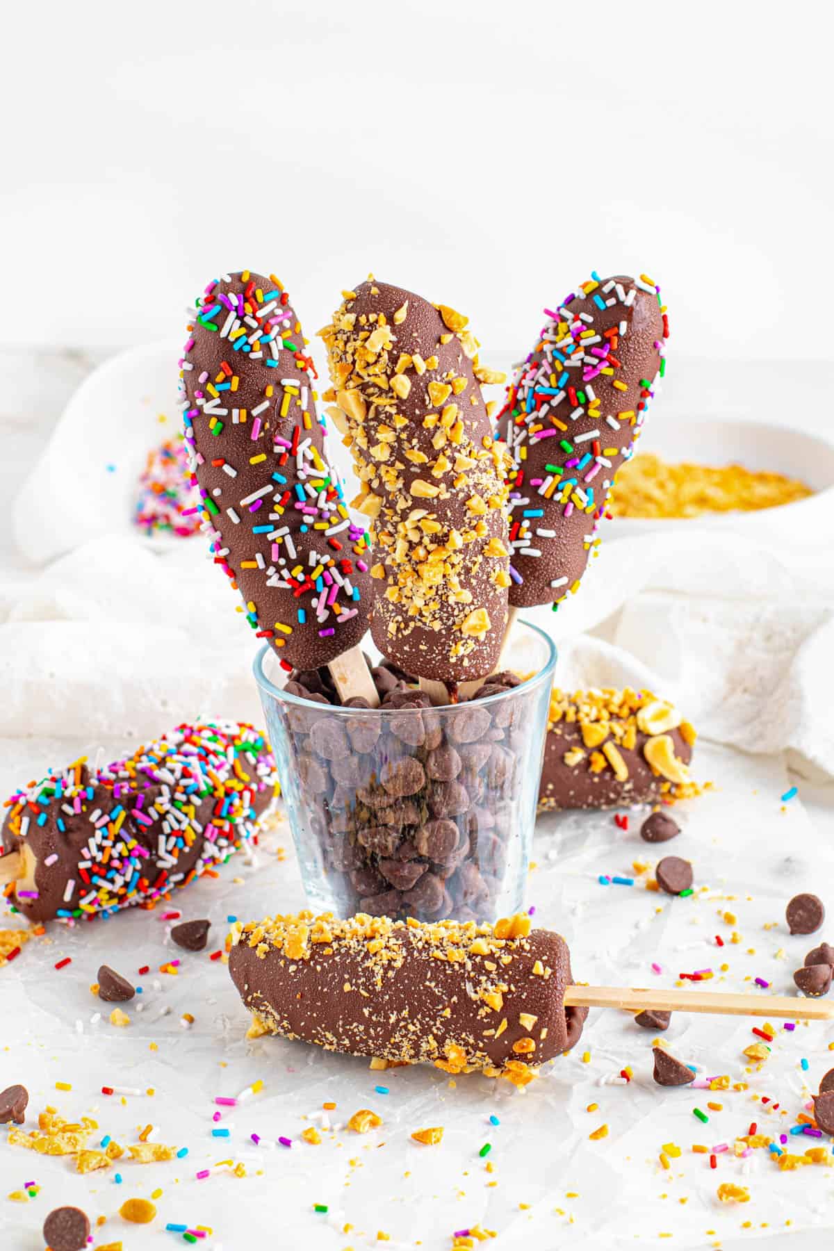 Frozen bananas with different toppings sticking up out of a cup of chocolate chips.