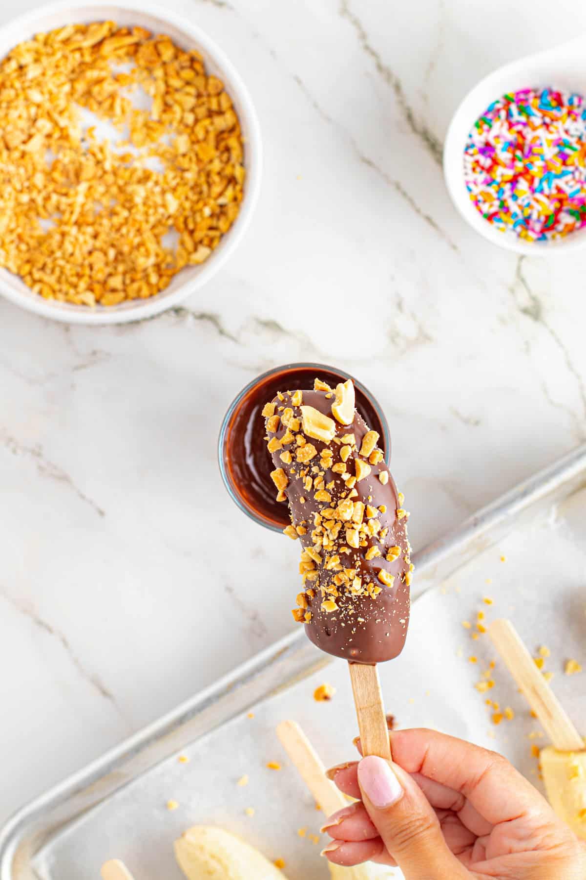 Adding chopped peanuts to a chocolate frozen banana.