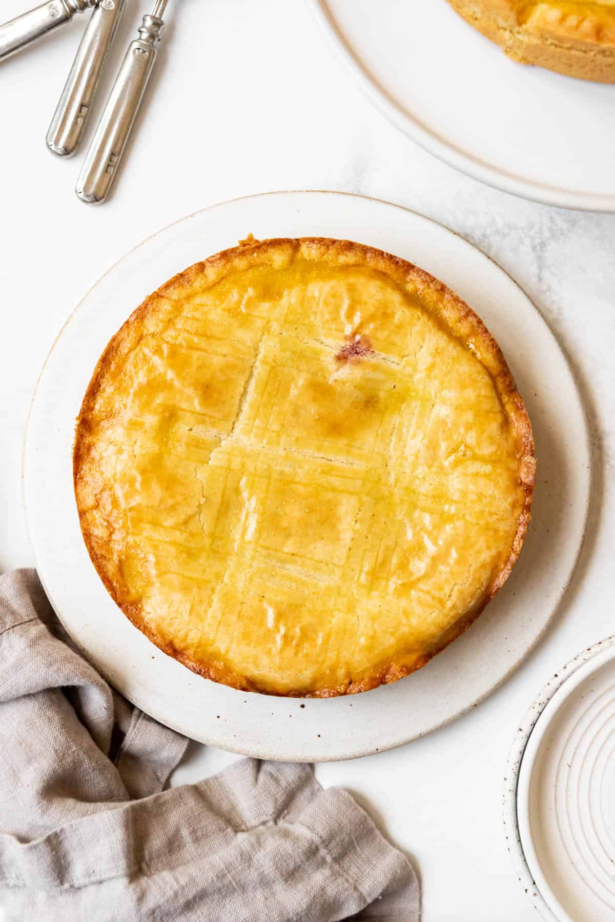 An image of a Gateau Basque cake on a white plate next to a cloth napkin.