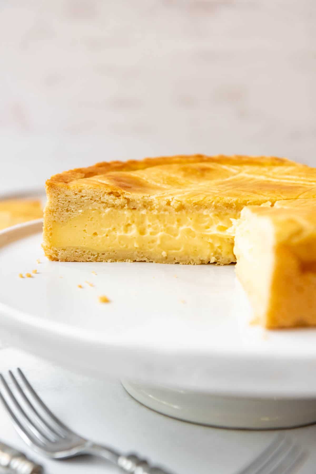 A partially sliced Gateau Basque cake on a white cake stand.