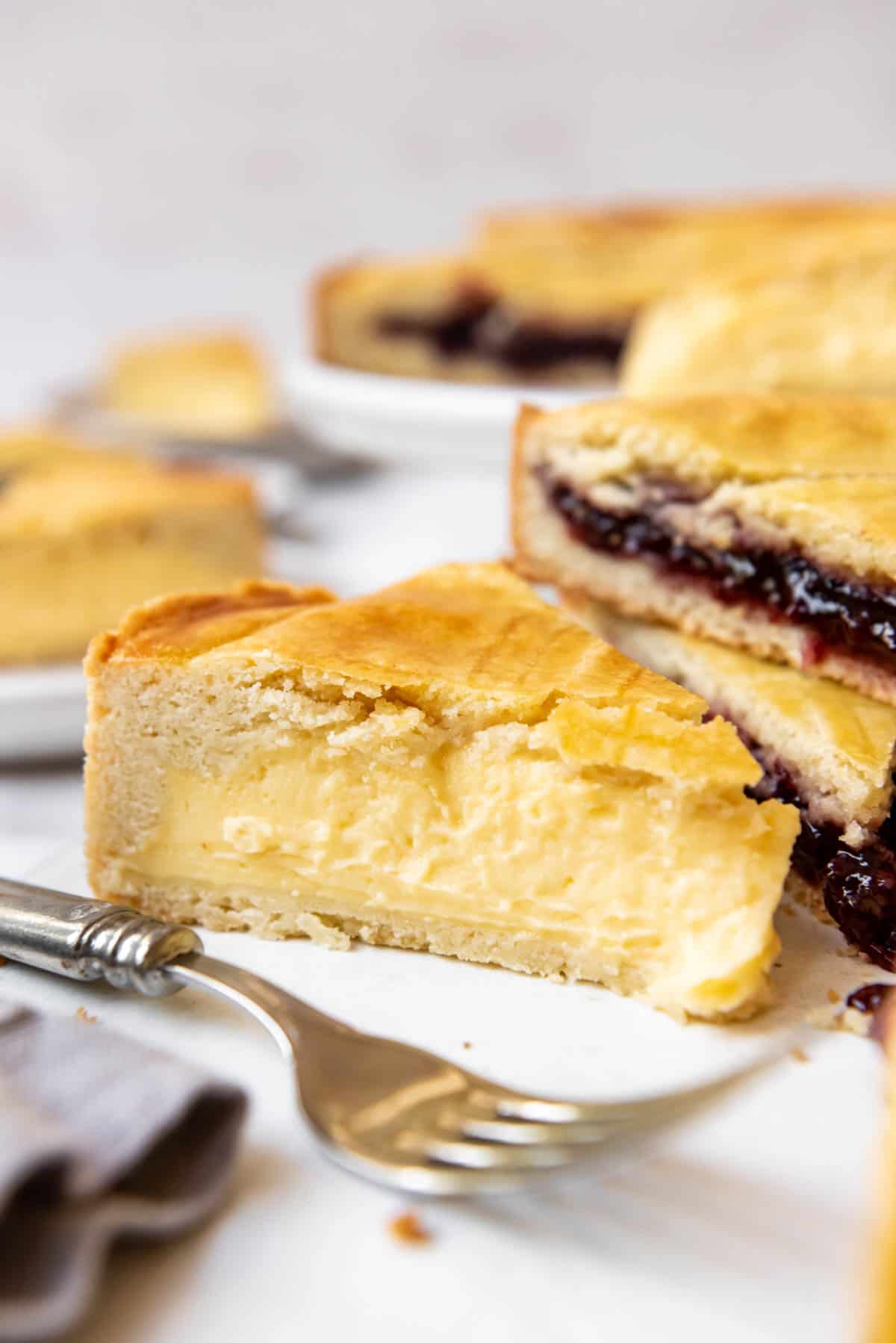 Slices of pastry cream and cherry jam filled Gateau Basque with a fork in front of them.