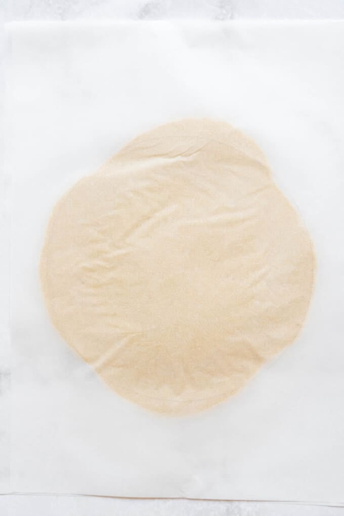 Rolling out Gateau Basque pastry crust between two sheets of parchment paper.