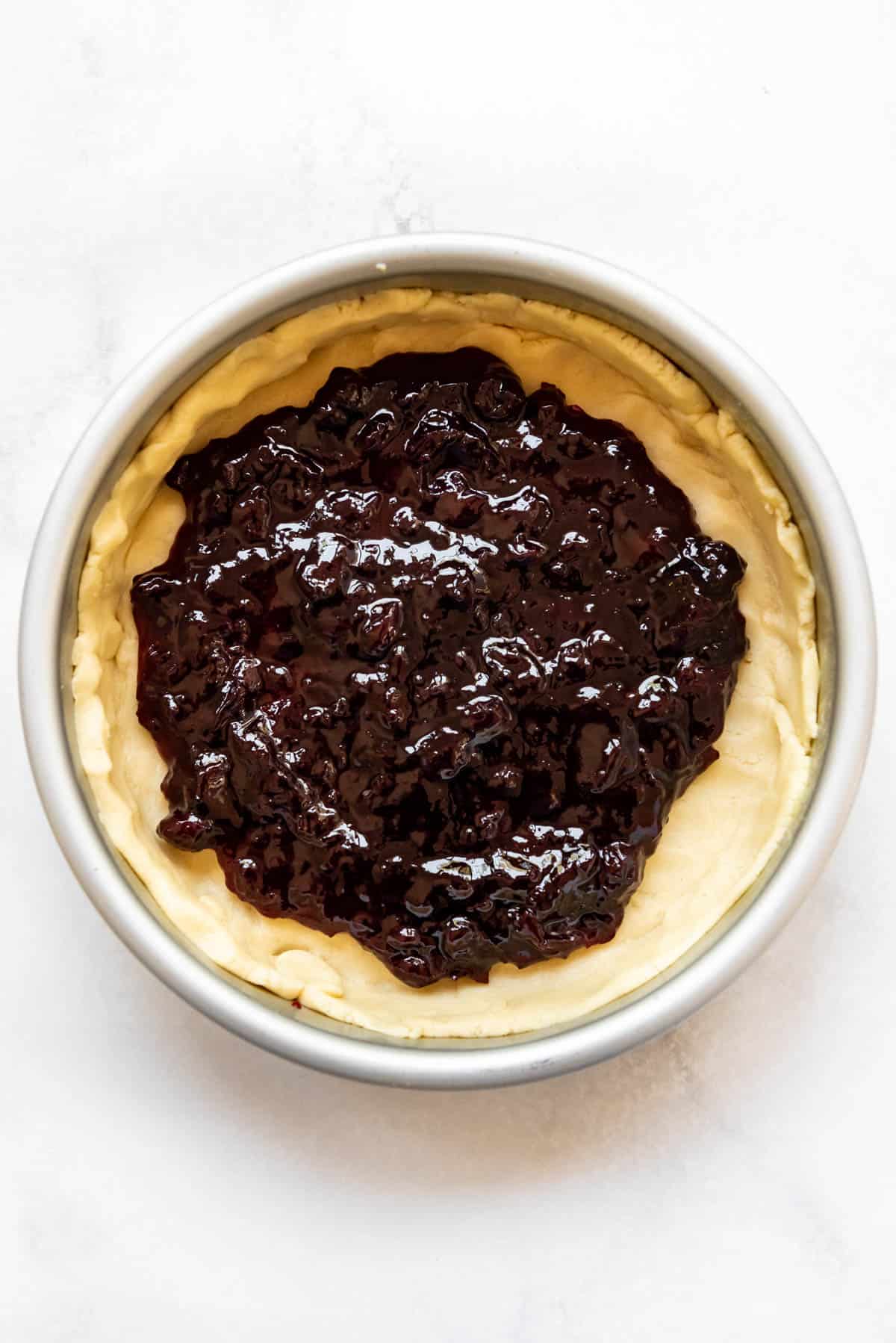 Sweet pastry crust in a cake pan filled with cherry jam.