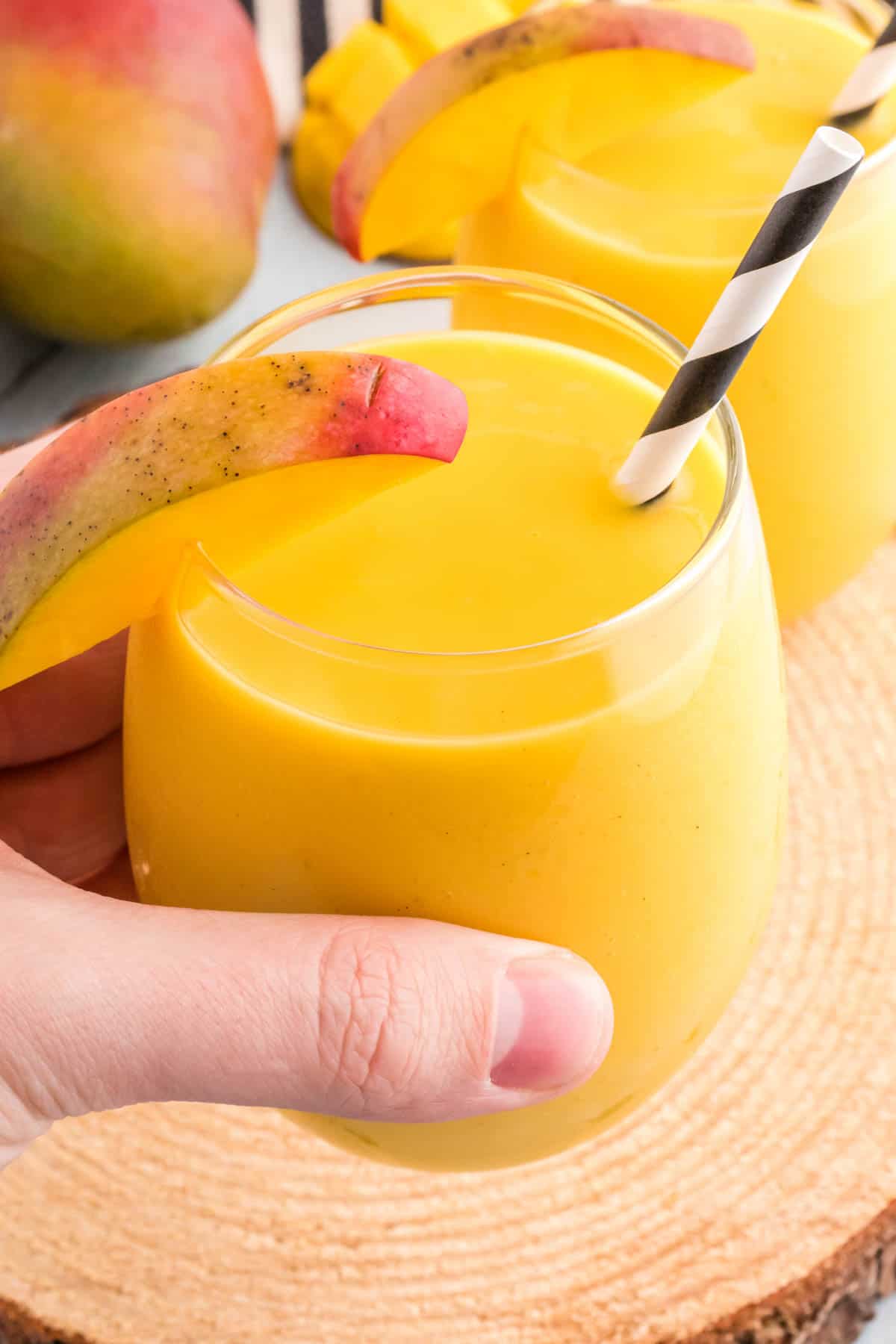 A hand lifting a glass of mango lassi drink.