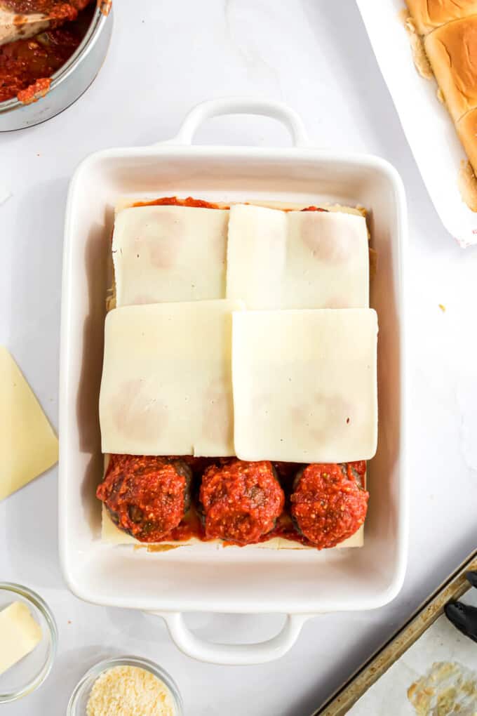 Topping meatballs with more sliced cheese for sliders.