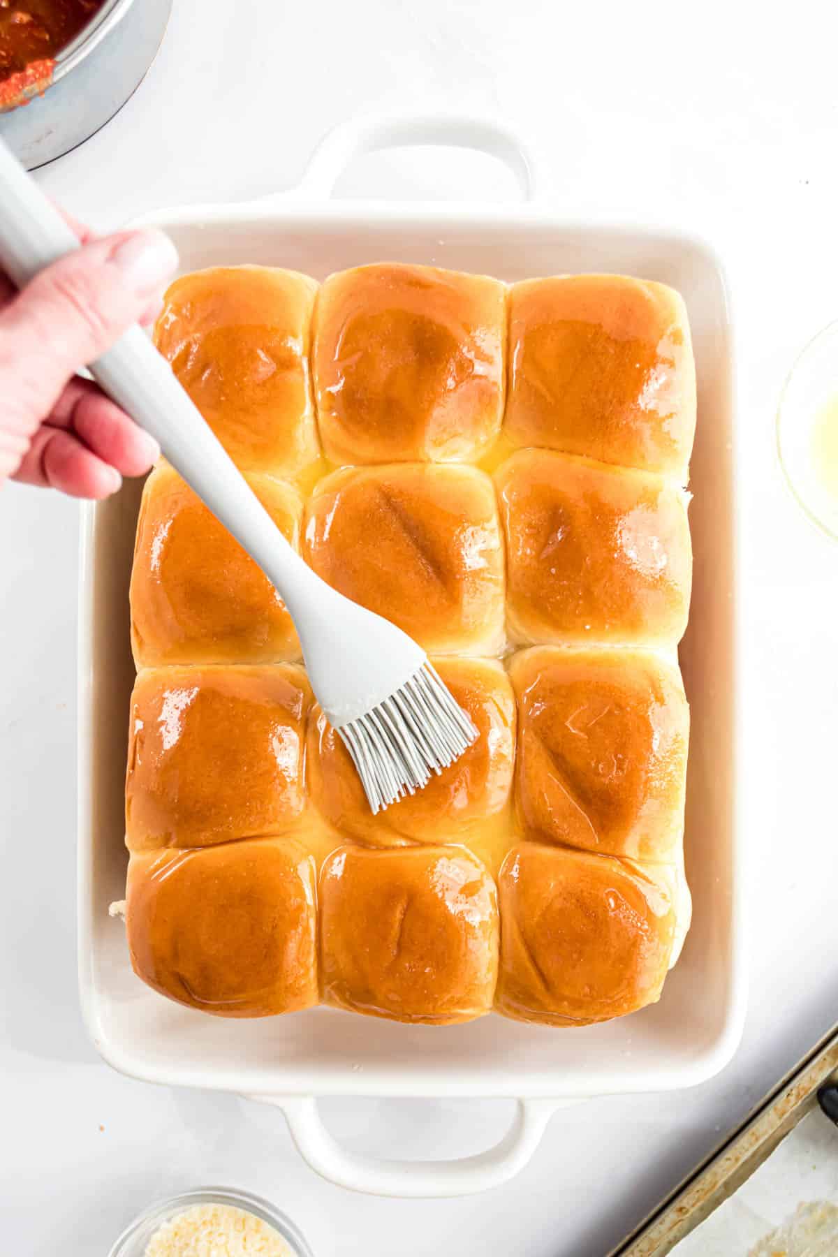 Brushing melted butter over slider buns.