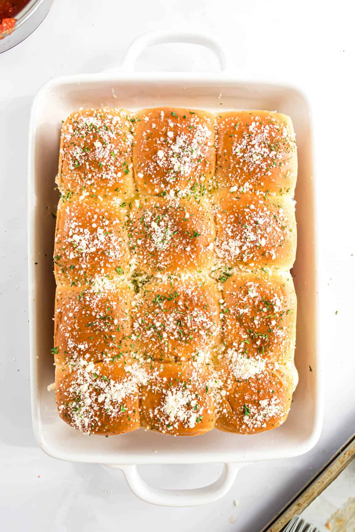 Sprinkling parmesan cheese and herbs over meatball sliders.