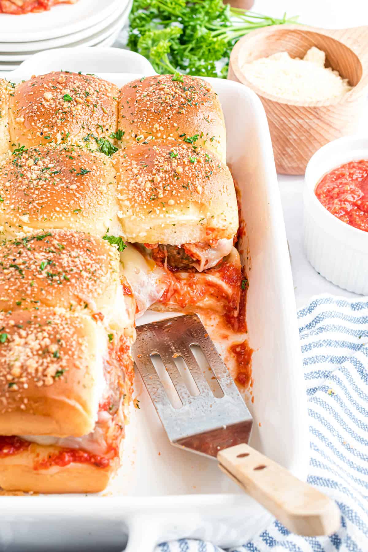 A pan of meatball sliders with a spatula in it.