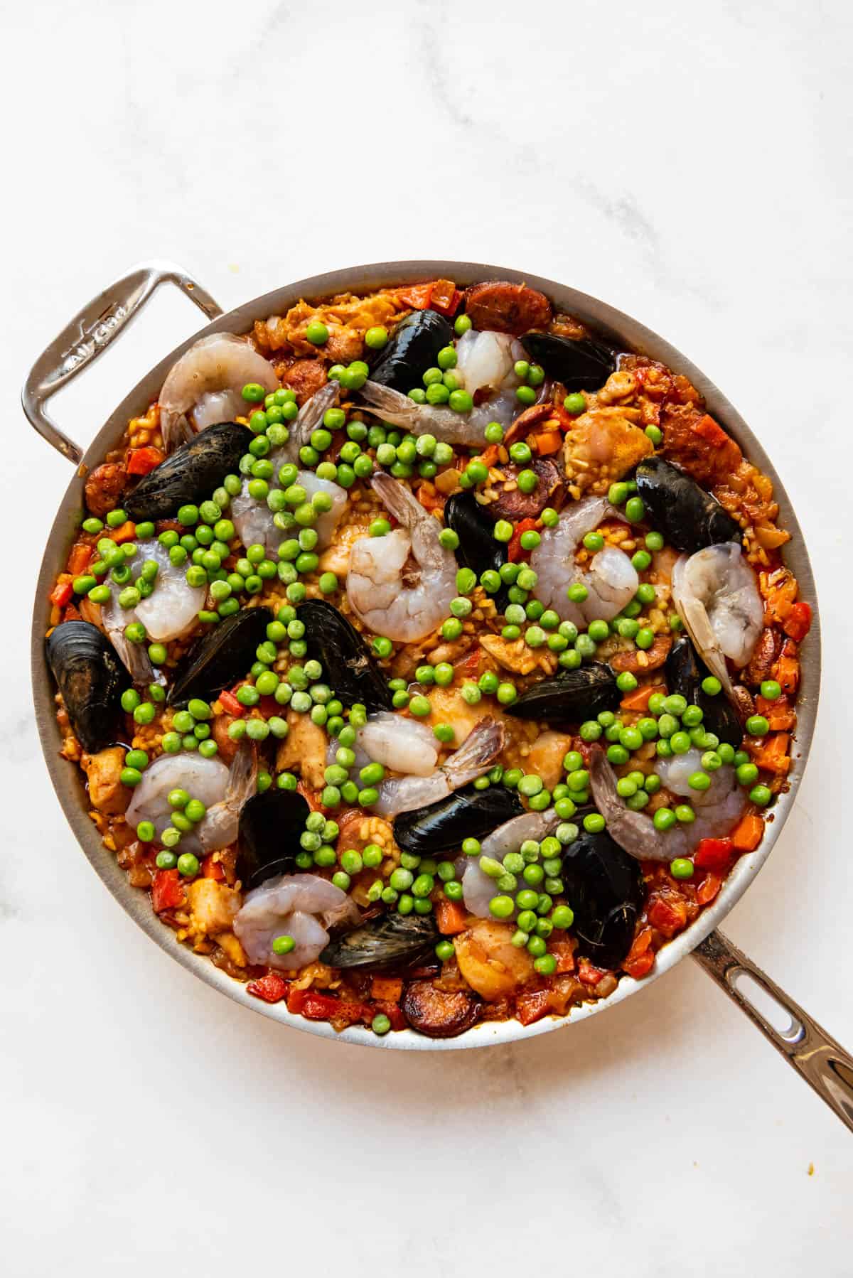 Adding raw shrimp and mussels and peas to paella.