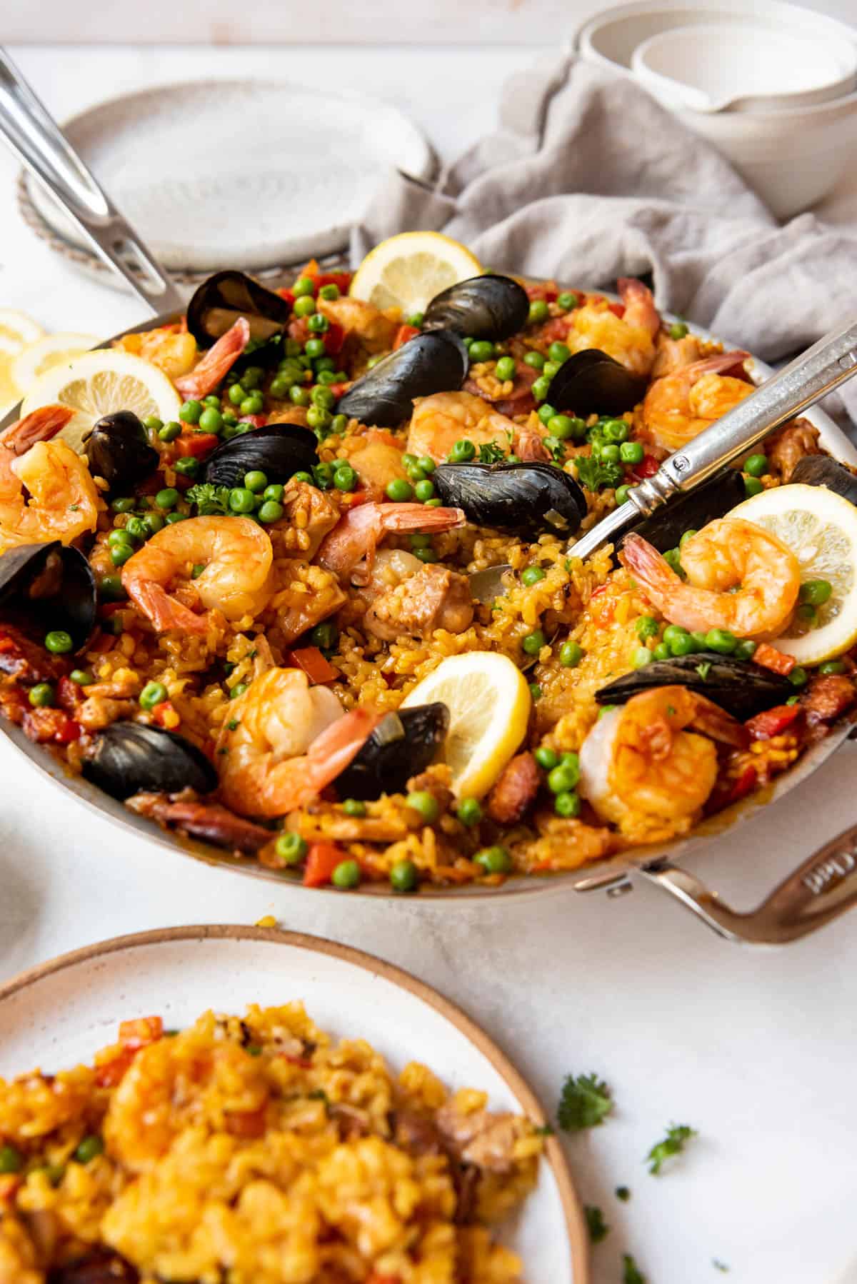 A pan of mixed Spanish paella with a serving spoon in it next to a plate of paella.