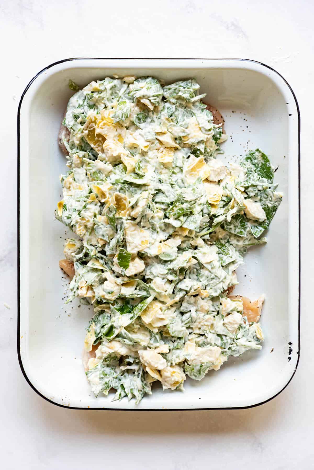 Spreading spinach artichoke mixture over chicken breasts in a baking dish.