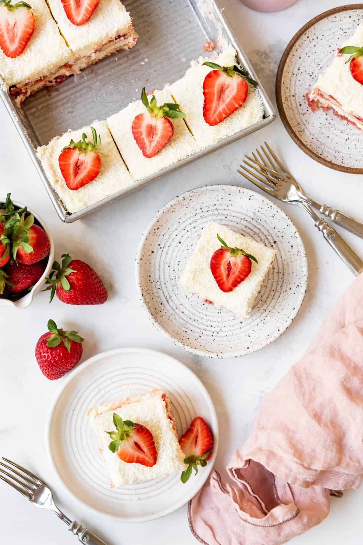An overhead image of slices of strawberry tiramisu on plates with strawberry halves on top.