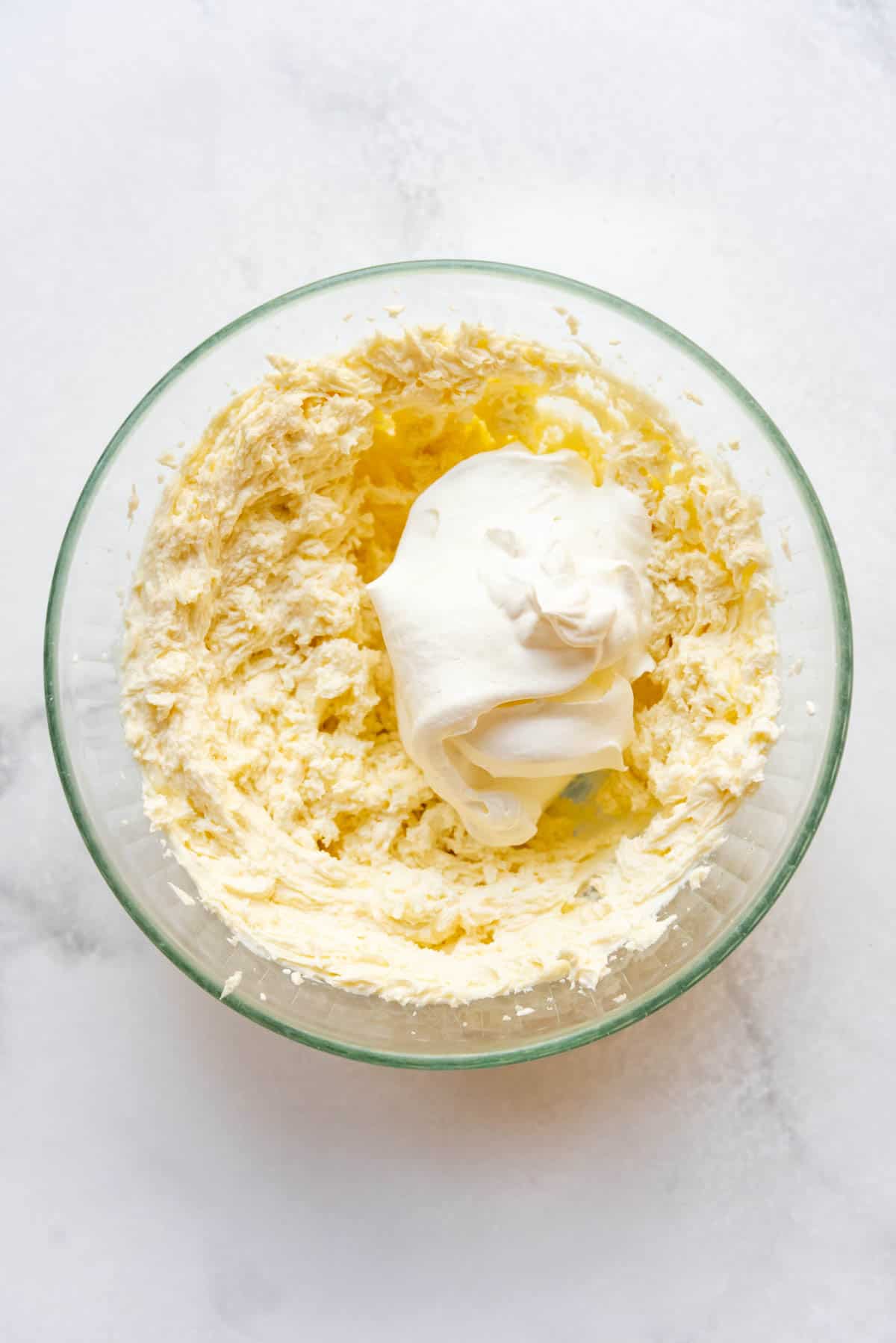 Adding whipped cream to a mascarpone cheese mixture in a glass mixing bowl.