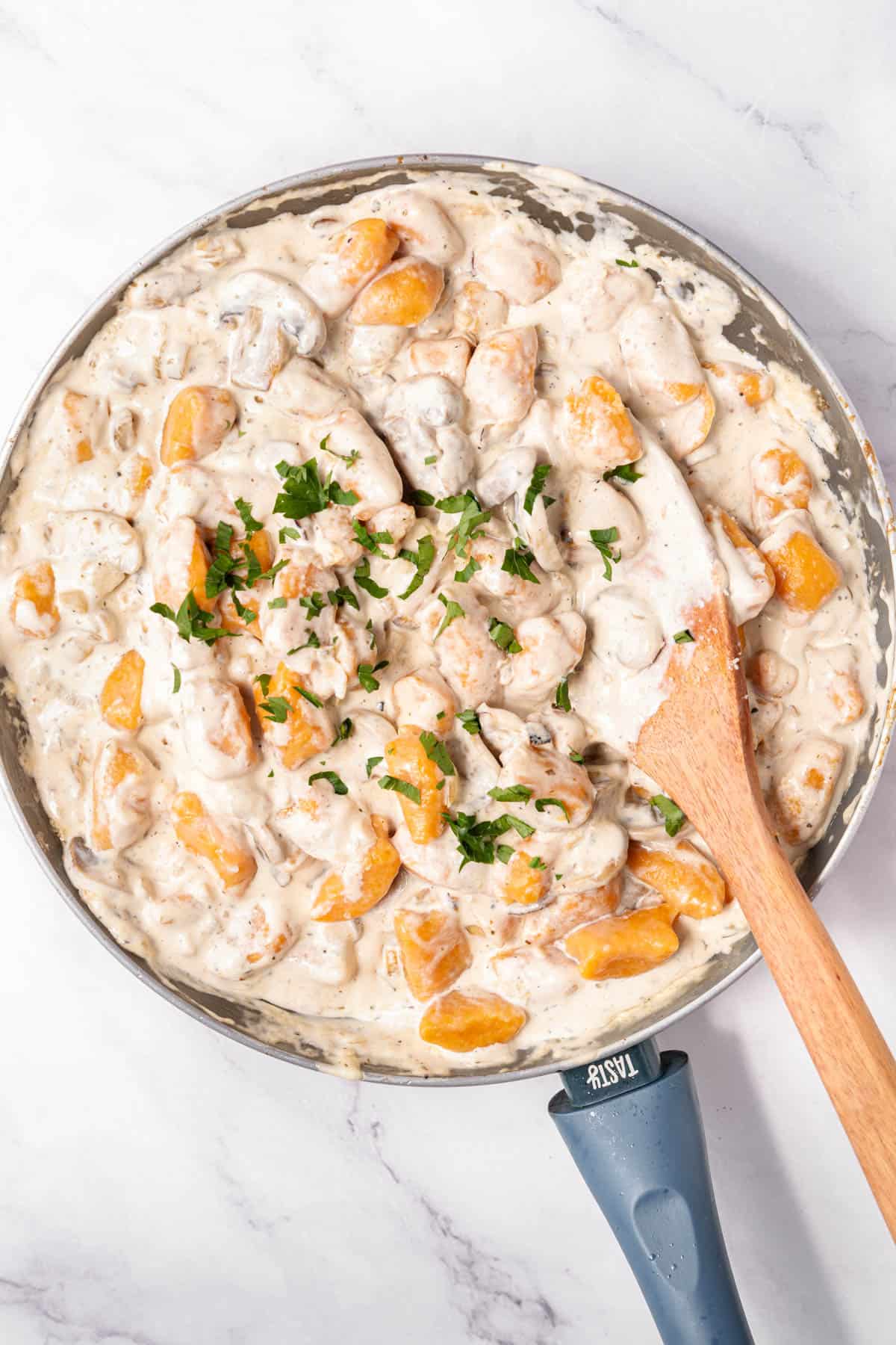 Finished sweet potato gnocchi in a large pan of creamy mushroom sauce.