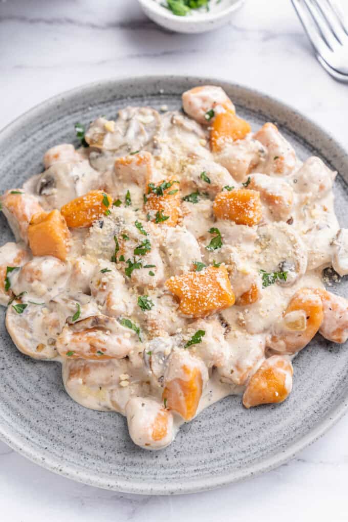 An image of sweet potato gnocchi in a creamy mushroom sauce on a blue plate.