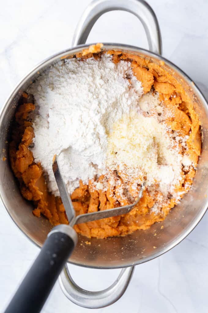 Adding flour and parmesan cheese to mashed sweet potatoes.