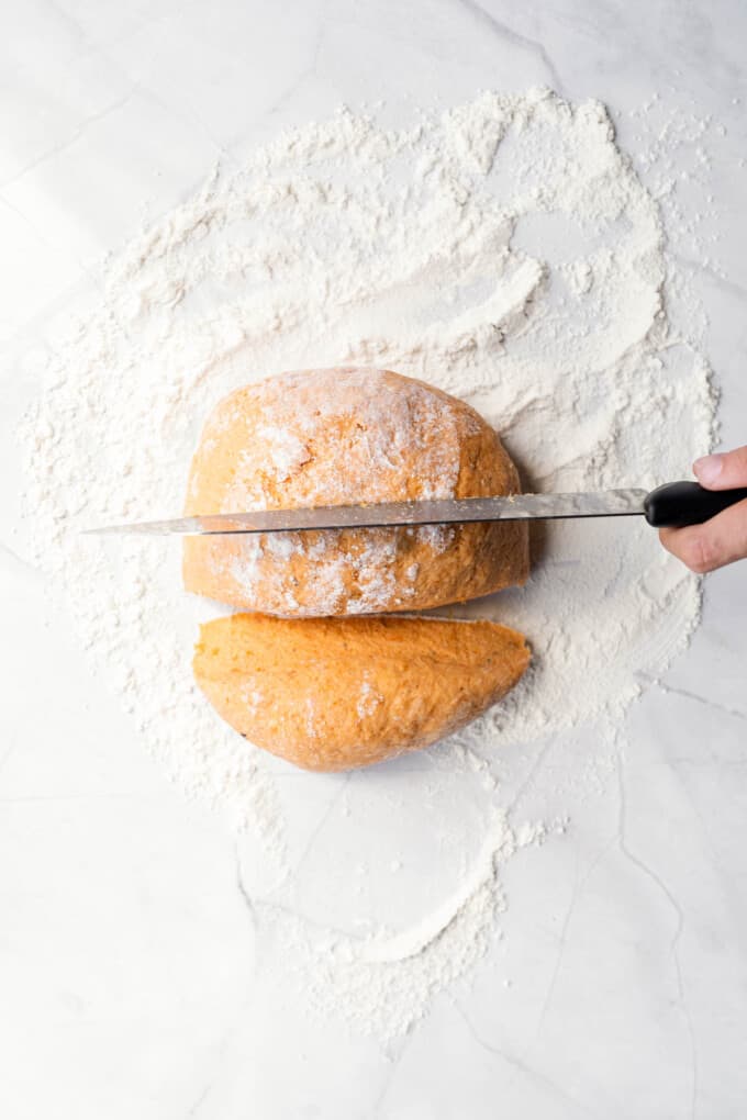 Dividing sweet potato gnocchi dough into thirds with a sharp knife on a floured surface.
