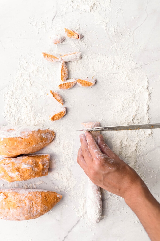Cutting a rope of sweet potato gnocchi dough on a floured surface.