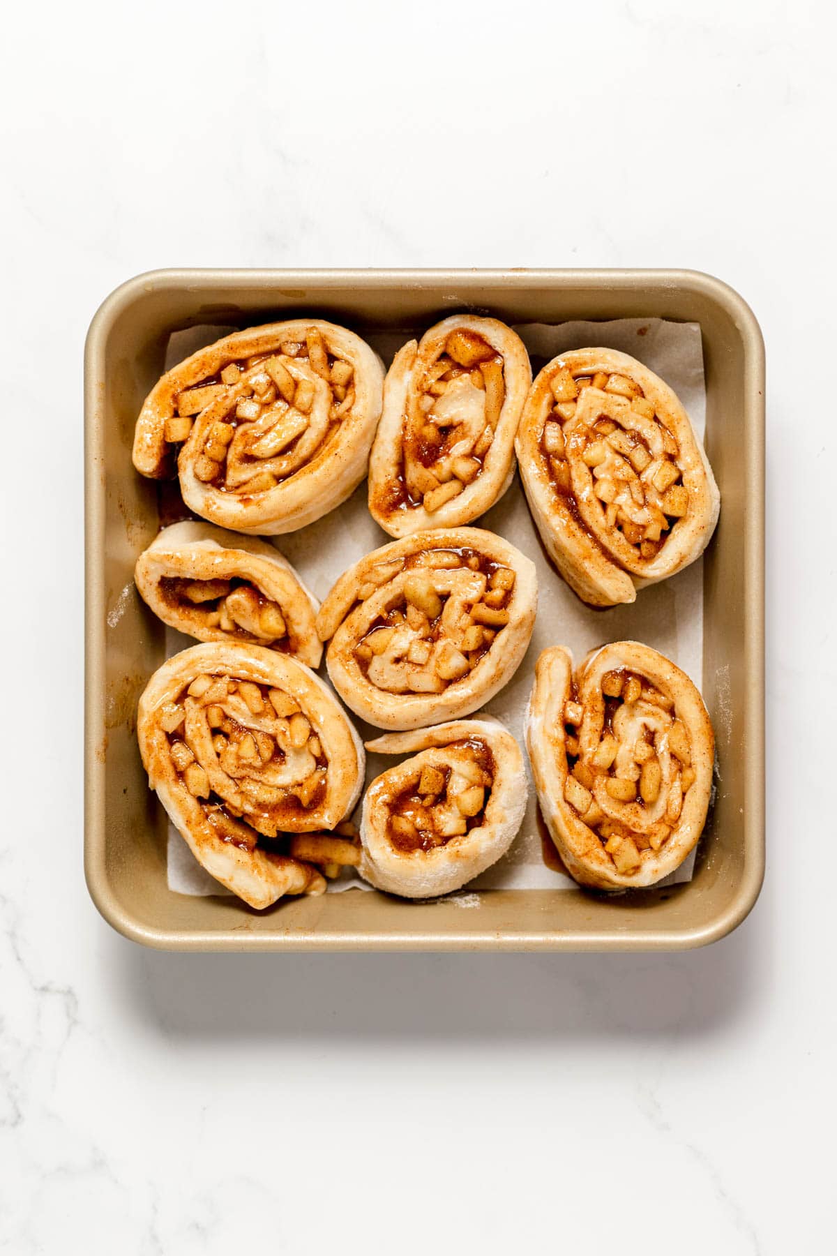 Arranging apple cinnamon rolls in a square metal baking dish.