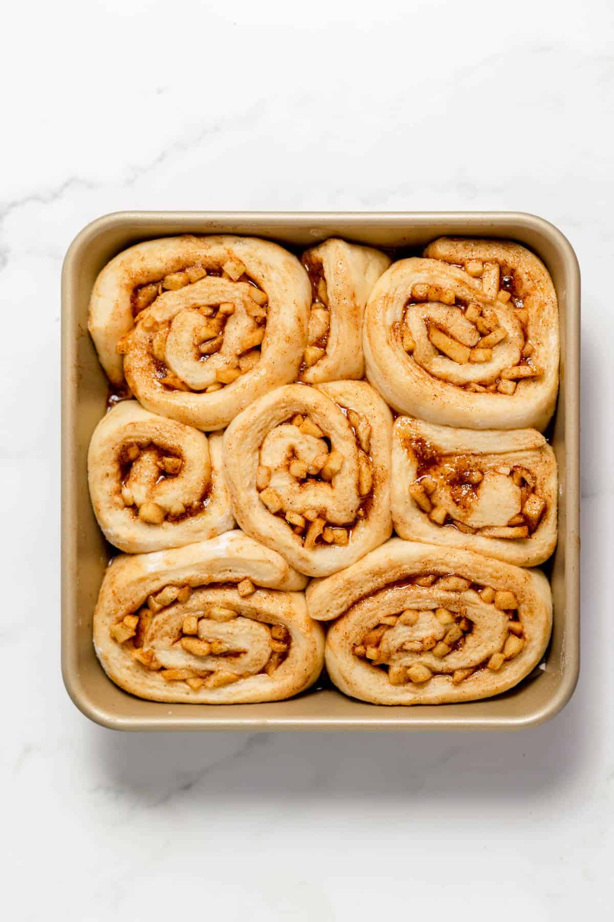 Puffy apple cinnamon rolls in a pan ready to bake.