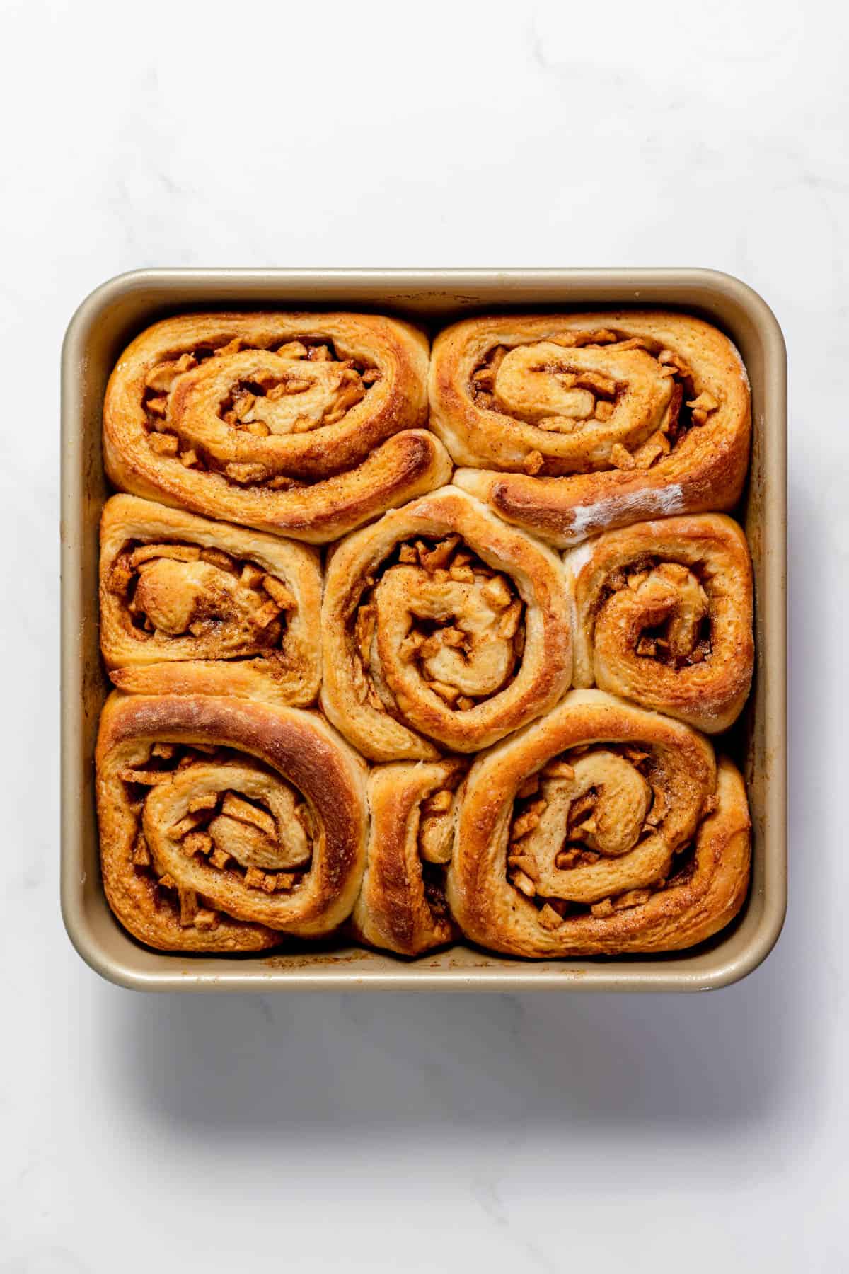 Baked apple cinnamon rolls in a square baking dish.