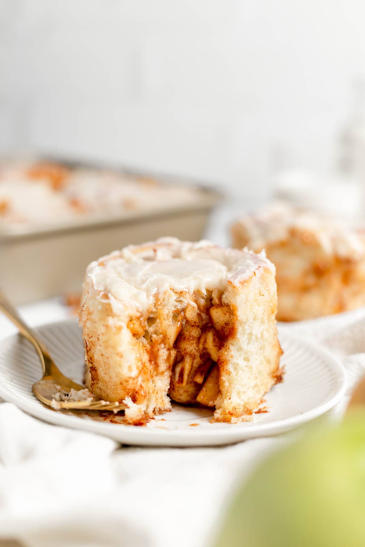 An apple cinnamon roll on a white plate with a fork.