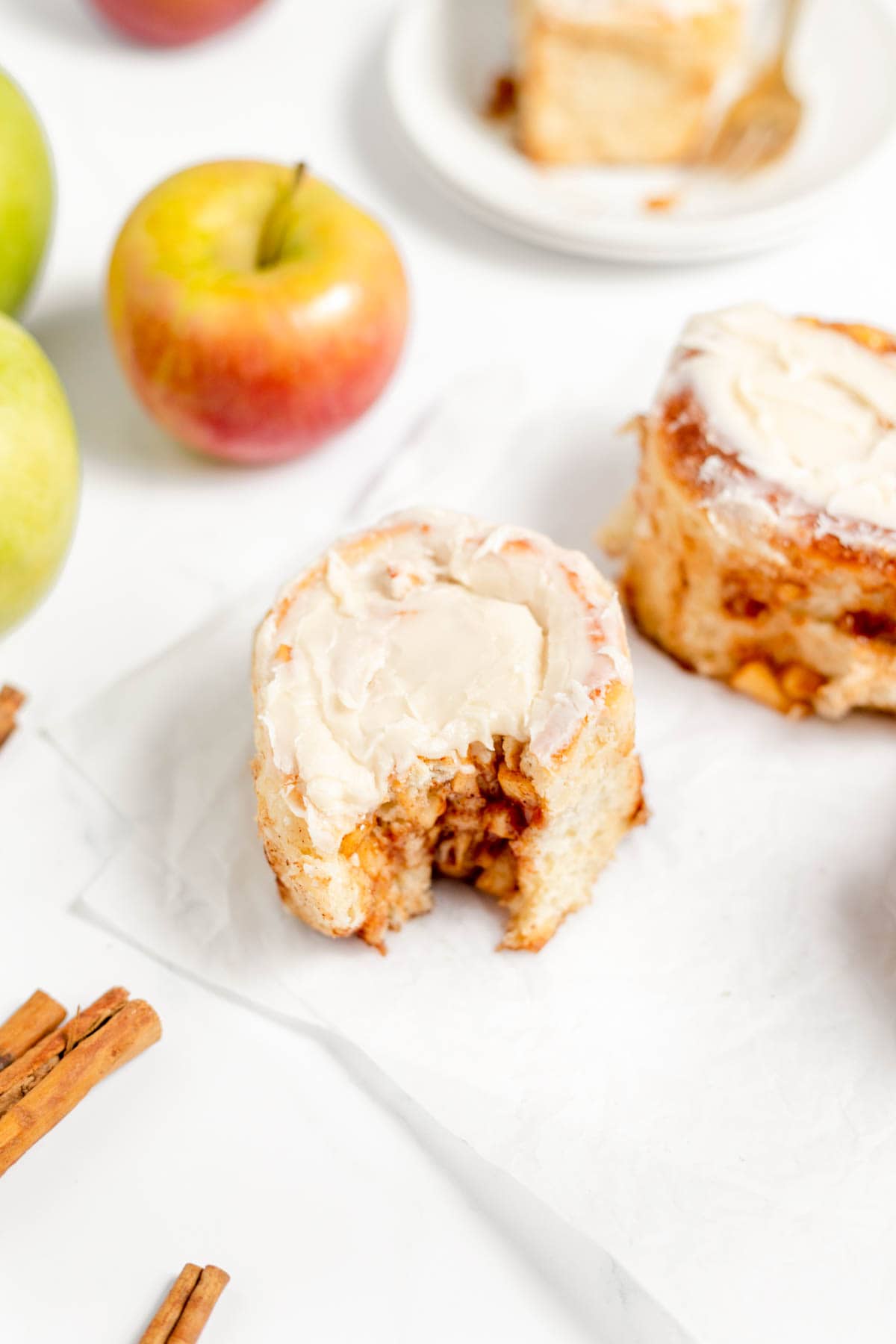 Gooey homemade apple cinnamon rolls on parchment paper with a bite taken out of one of them.