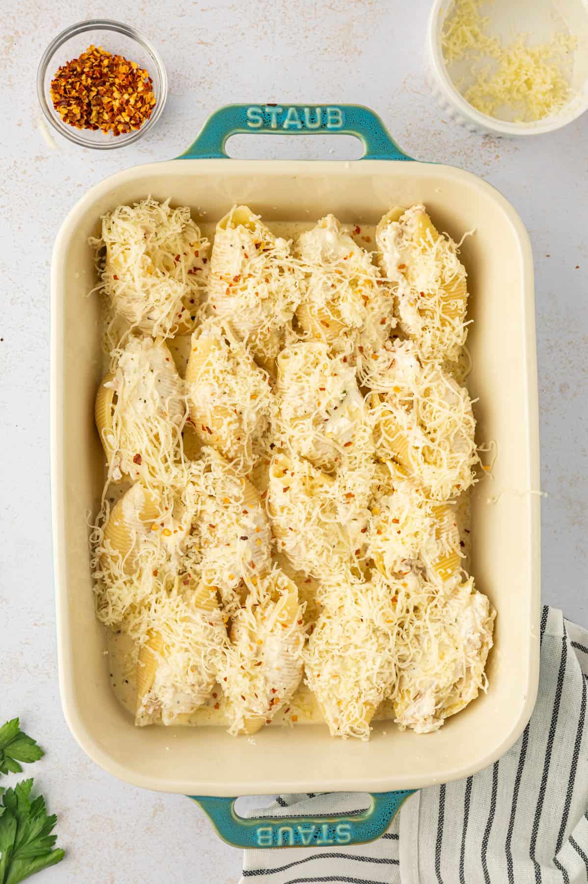 Topping chicken stuffed shells with freshly grated cheese before baking in the oven.