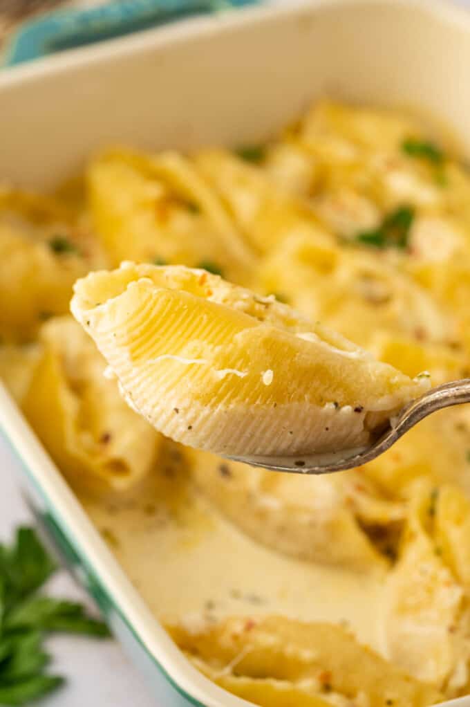 A spoon lifting a baked pasta shell stuffed with chicken and ricotta cheese.