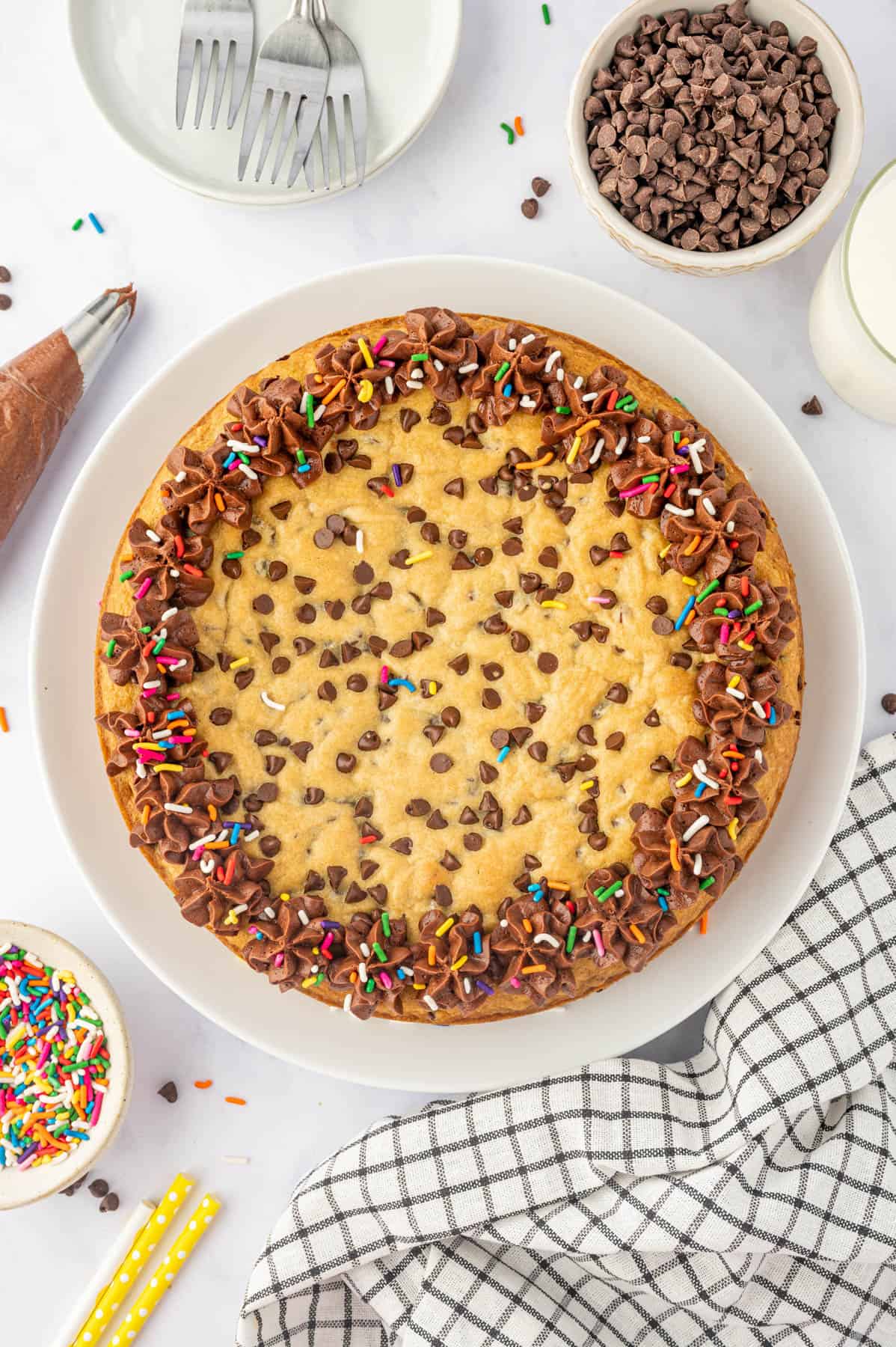 An overhead image of a chocolate chip cookie cake decorated with chocolate frosting and sprinkles.