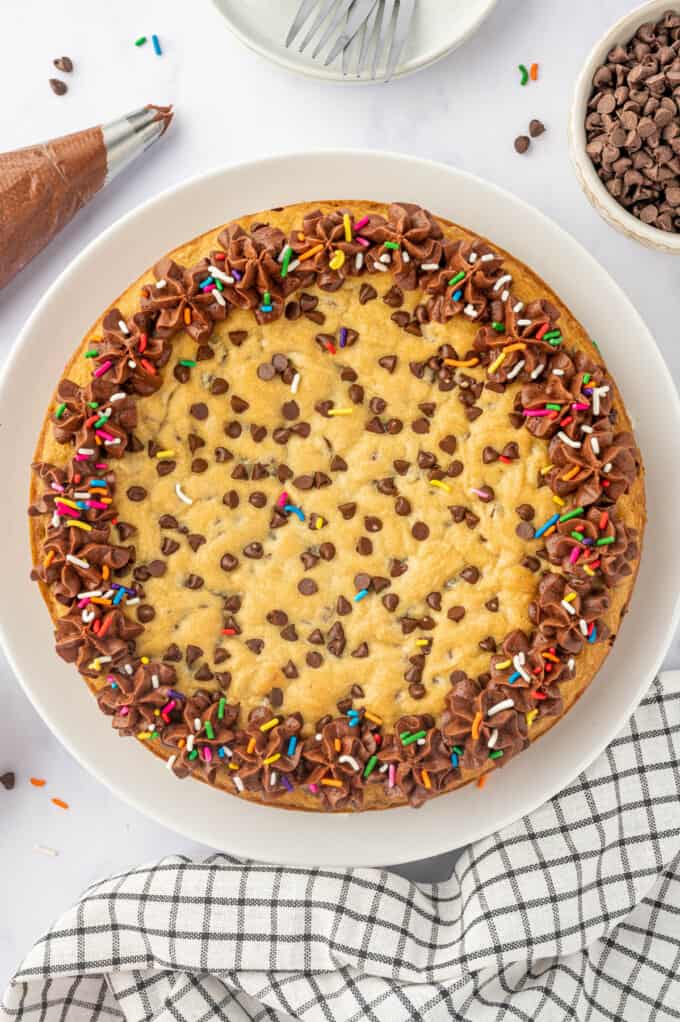 Decorating a chocolate chip cookie cake with chocolate frosting and sprinkles.