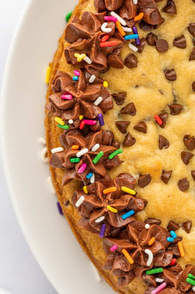 A close image of sprinkles on chocolate frosting on a chocolate chip cookie cake.
